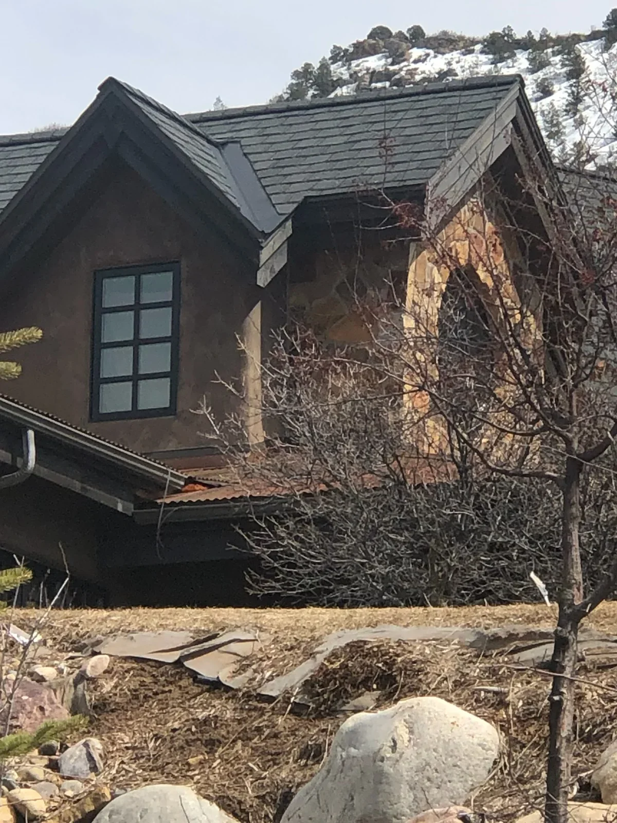 Dark stucco house with metal roof, grid windows, and hillside construction site