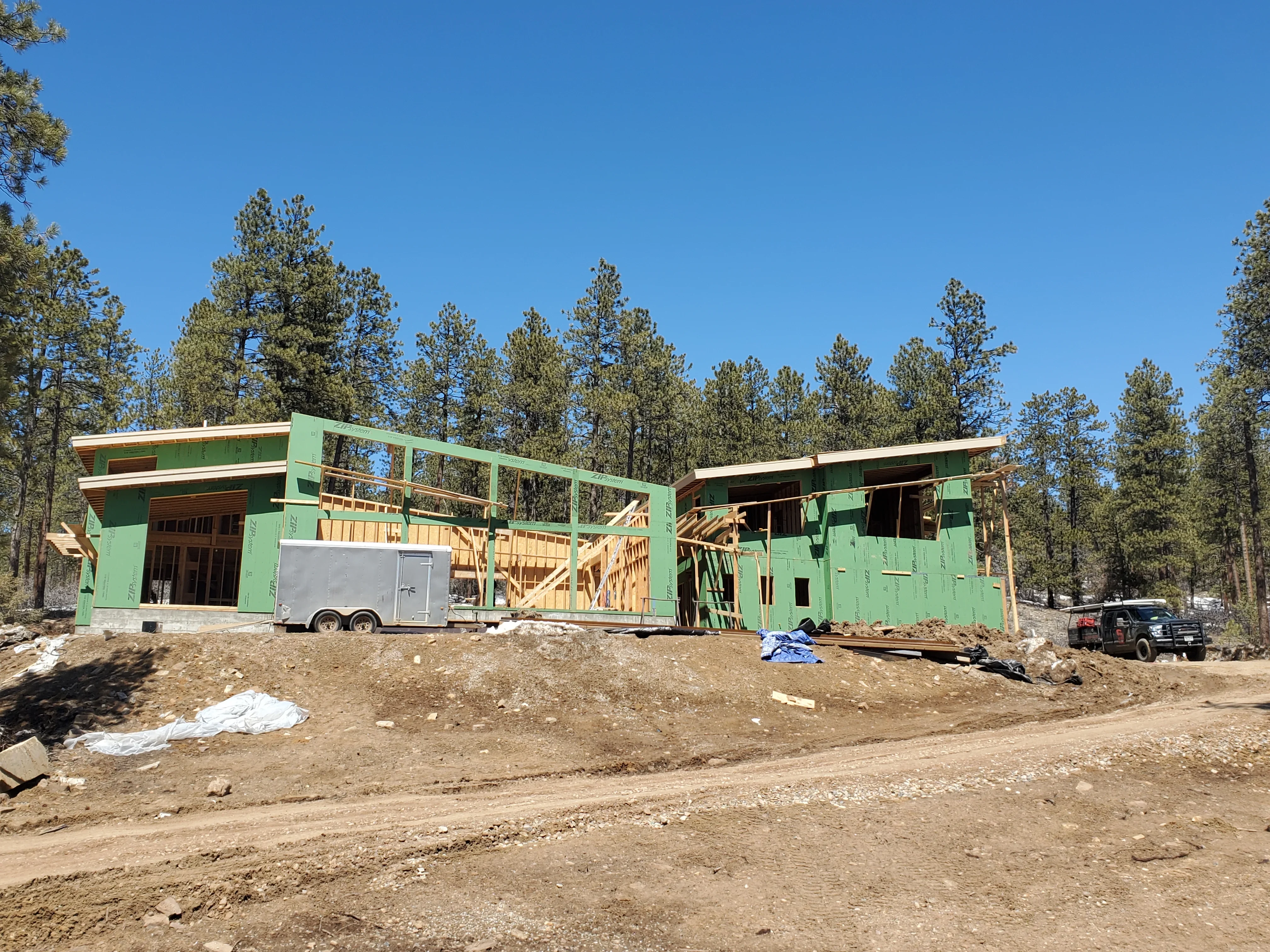 Green-wrapped residential framing structure with exposed wood beams and open floor plan under construction