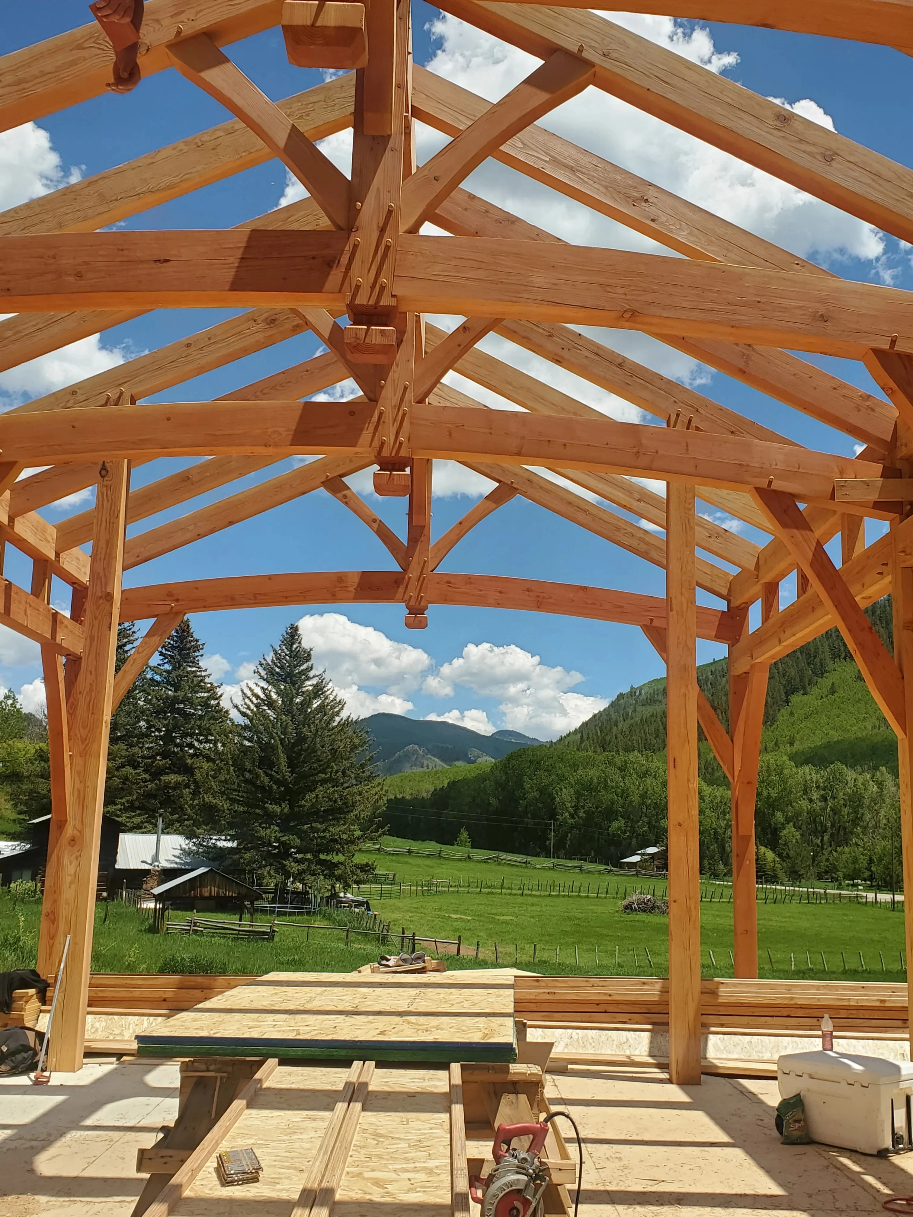 Timber frame pavilion with exposed beams, decorative trusses, and open roof framing under construction