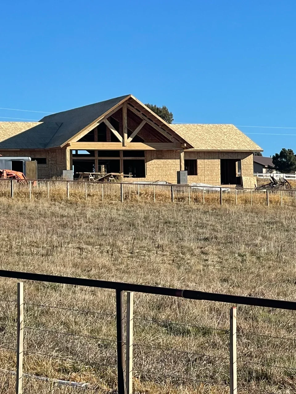 Residential home framing with timber trusses, OSB sheathing, and gable roof structure under construction