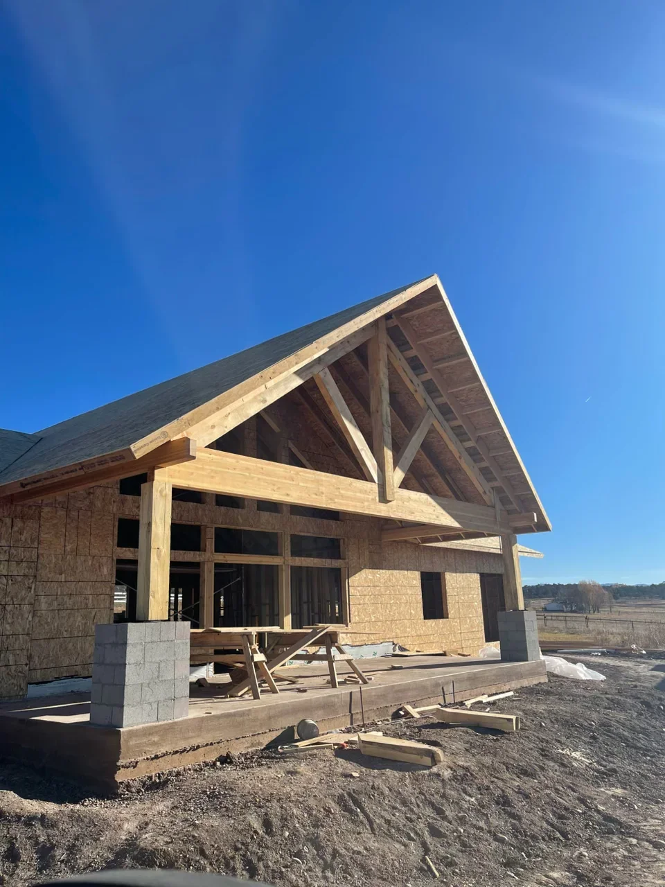 Timber frame house under construction with exposed beams, dimensional lumber framing, and concrete foundation