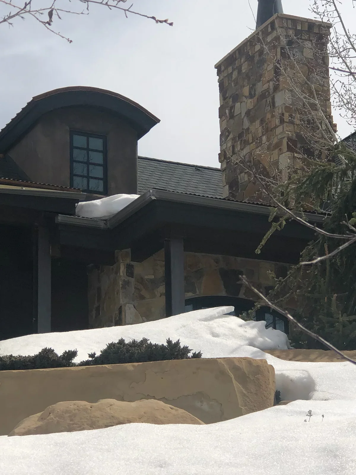 Stone chimney with slate roof, snow coverage, and dark exterior framing during restoration