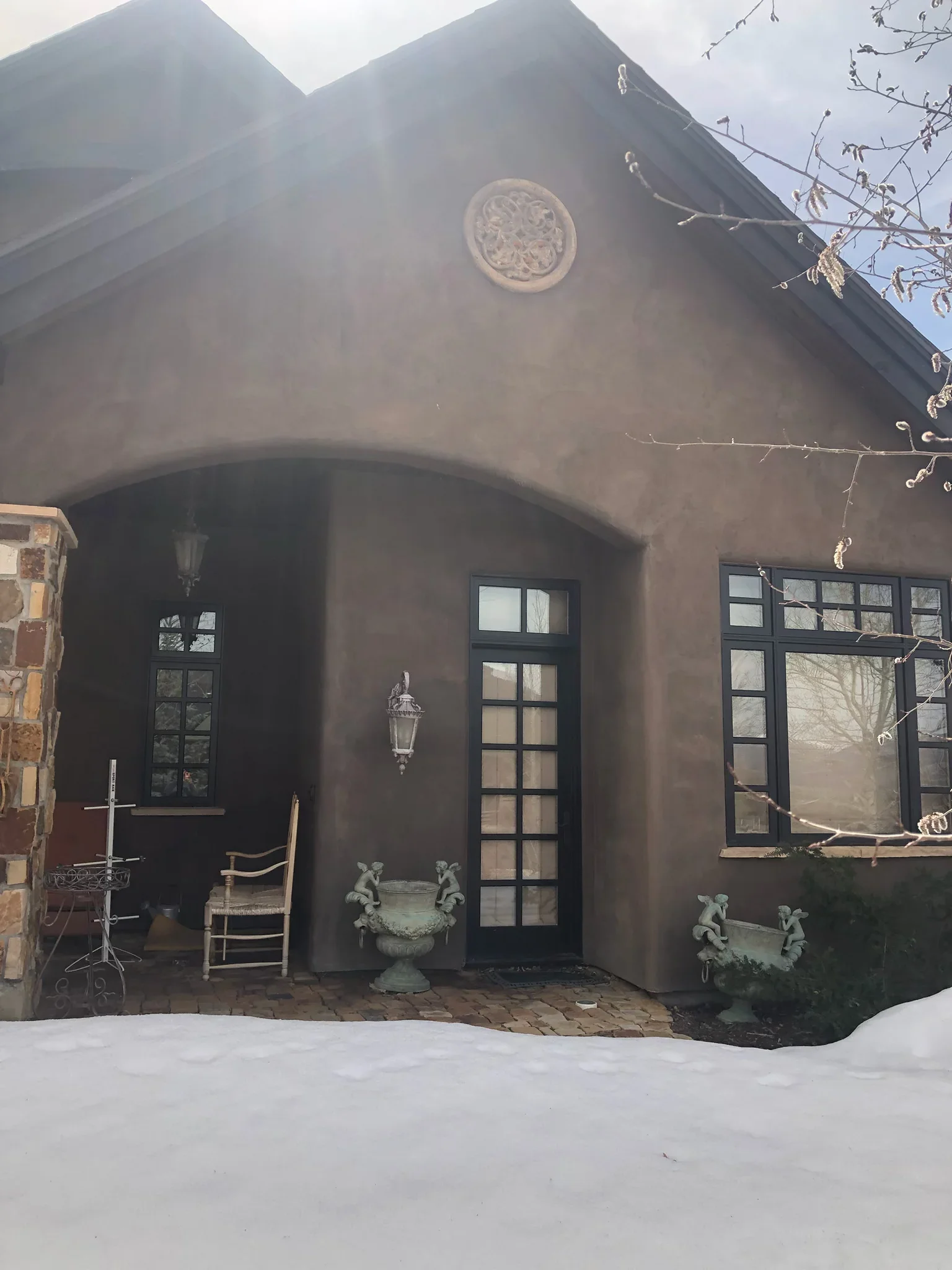 Dark stucco facade with curved archway, black French doors, and decorative medallion detail