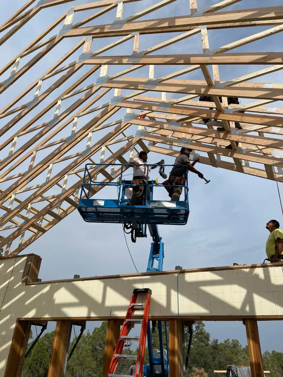 Roof framing installation with wooden trusses, metal connectors, and workers on lift platform