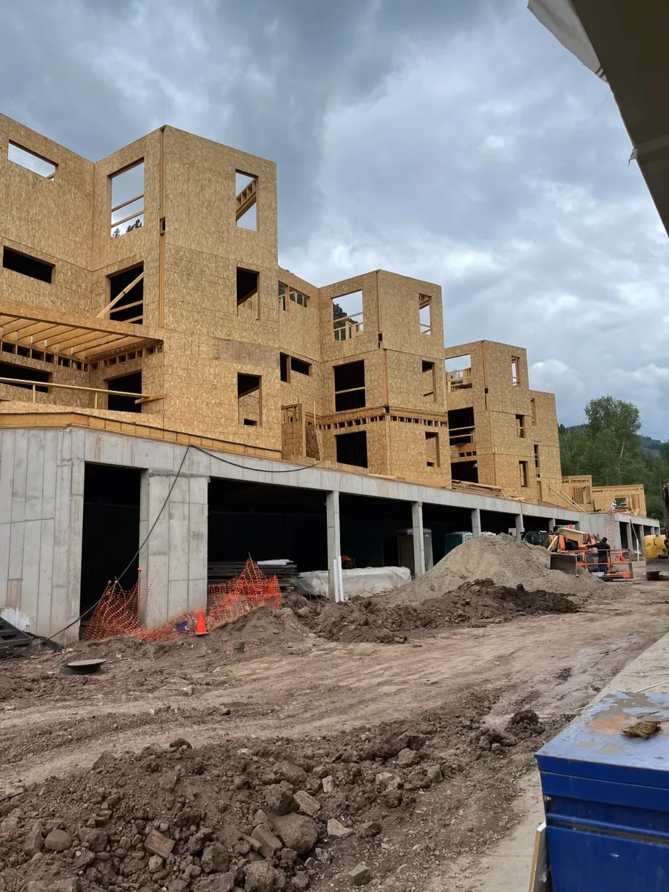 Multi-story residential framing with OSB sheathing, concrete foundation, and garage structure under construction