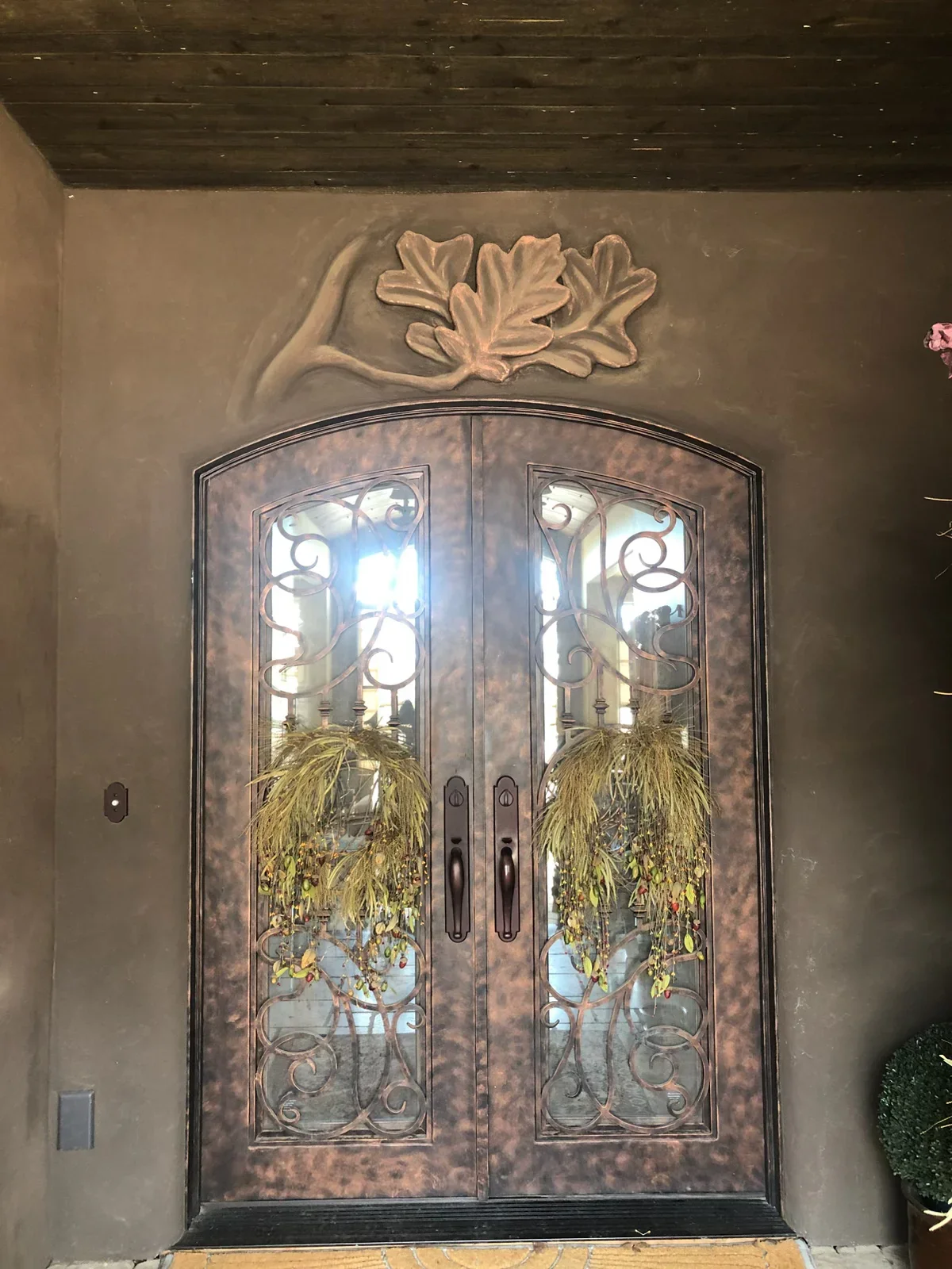 Custom arched double doors with iron scrollwork and glass panels in stucco surround