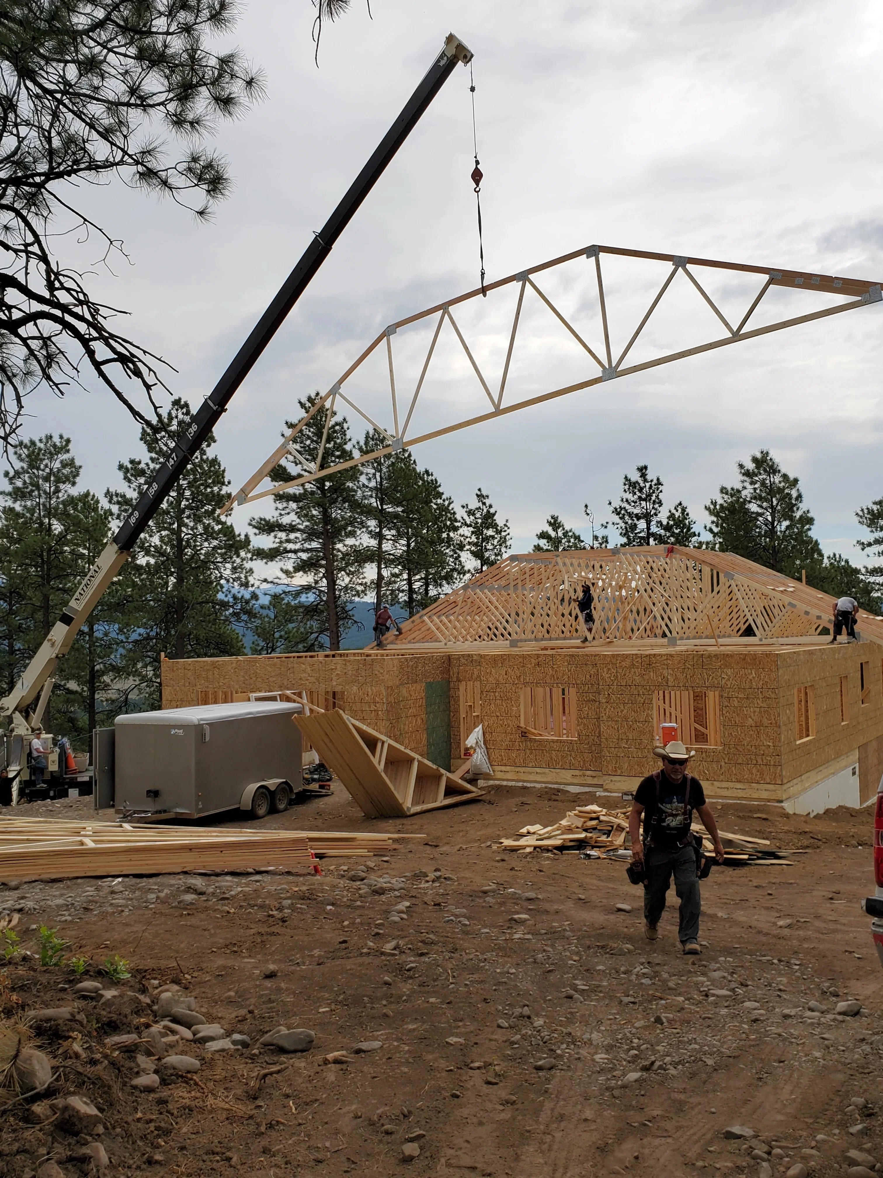 Crane lifting engineered roof truss over wood-framed residential structure with OSB sheathing