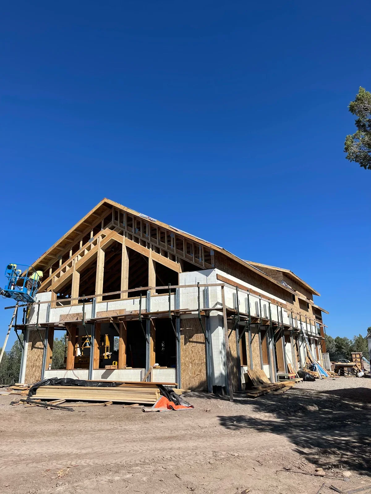 Two-story wood frame house under construction with exposed beams, joists, and roof trusses