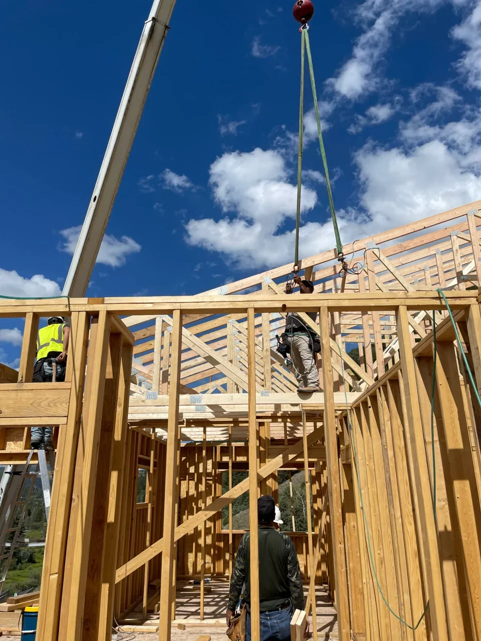 Wood framing structure with roof trusses, wall studs, and crane lifting materials during residential construction