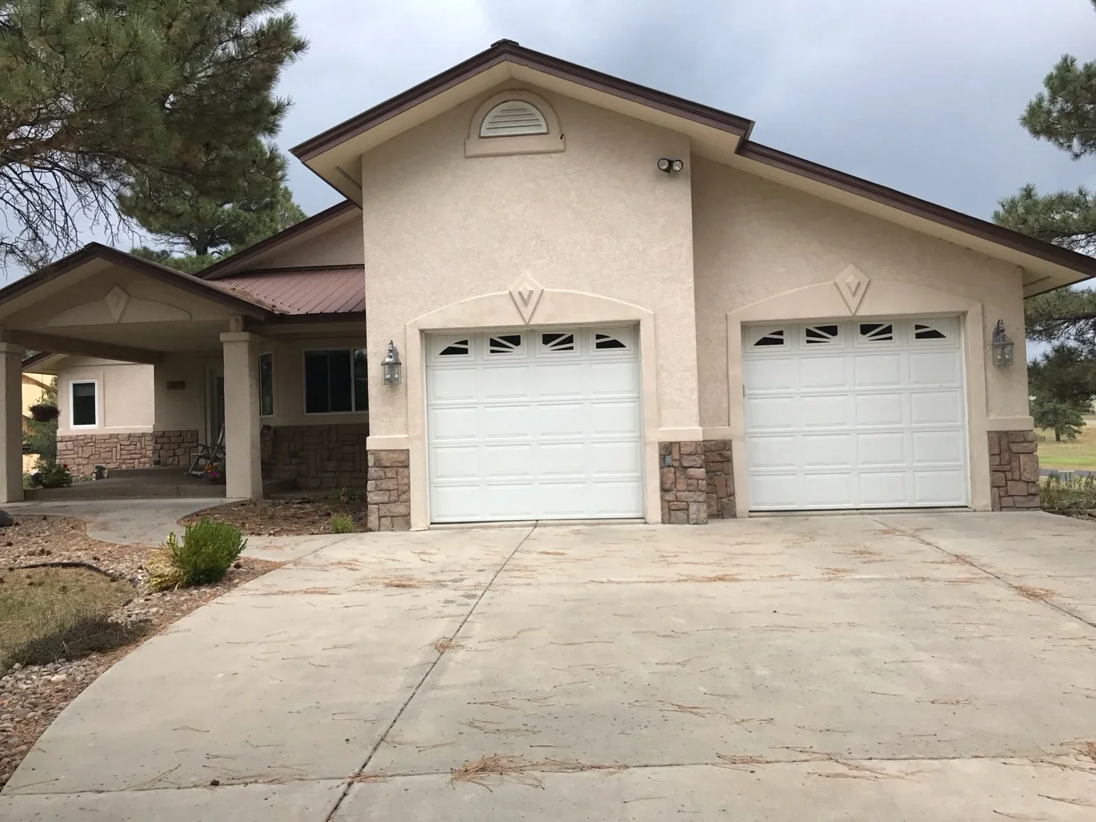 Cream stucco home with stone veneer base, two-car garage, covered porch, and concrete driveway