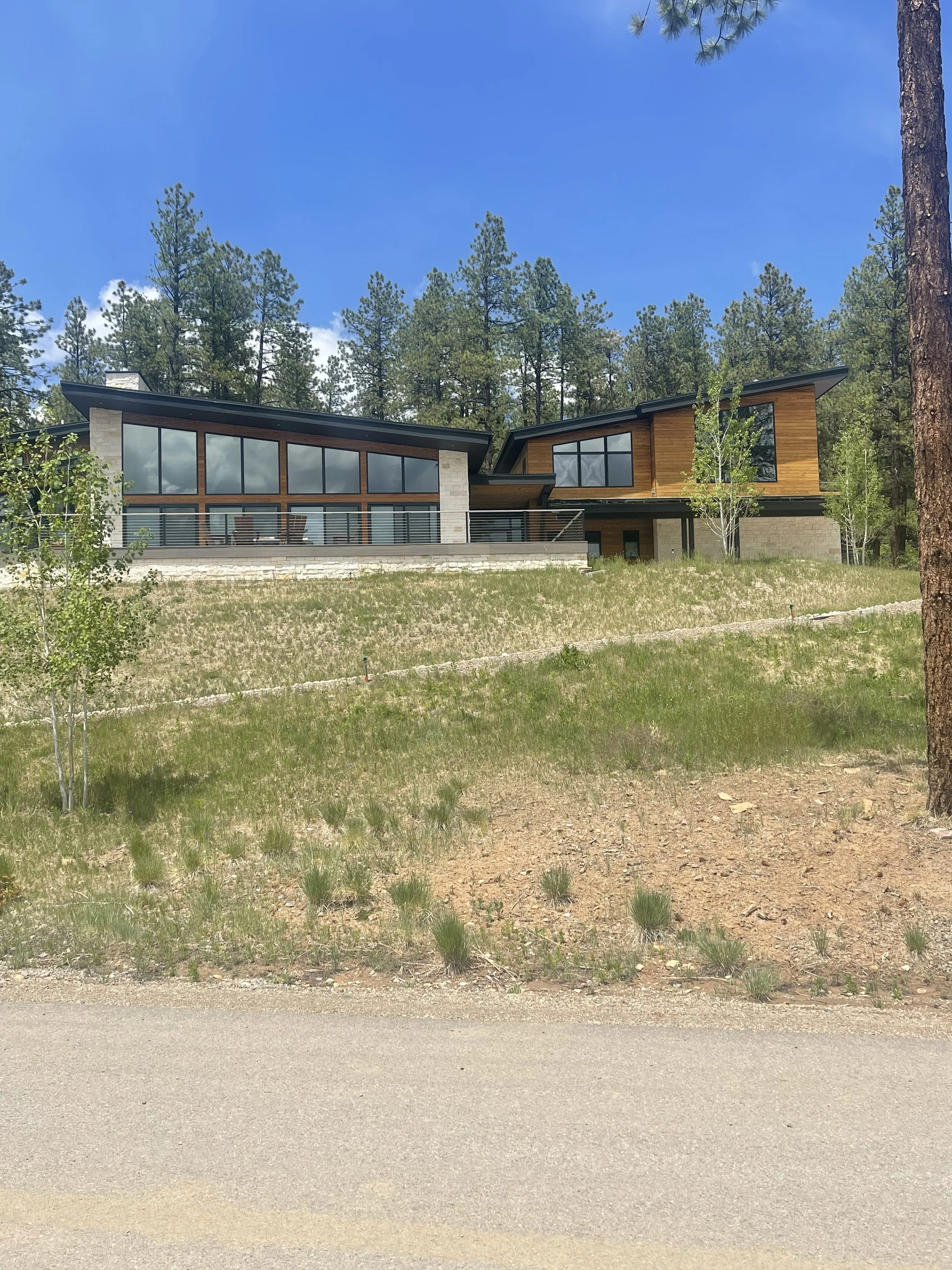 Modern home with stone base, cedar siding, metal railings, and large windows in forest setting