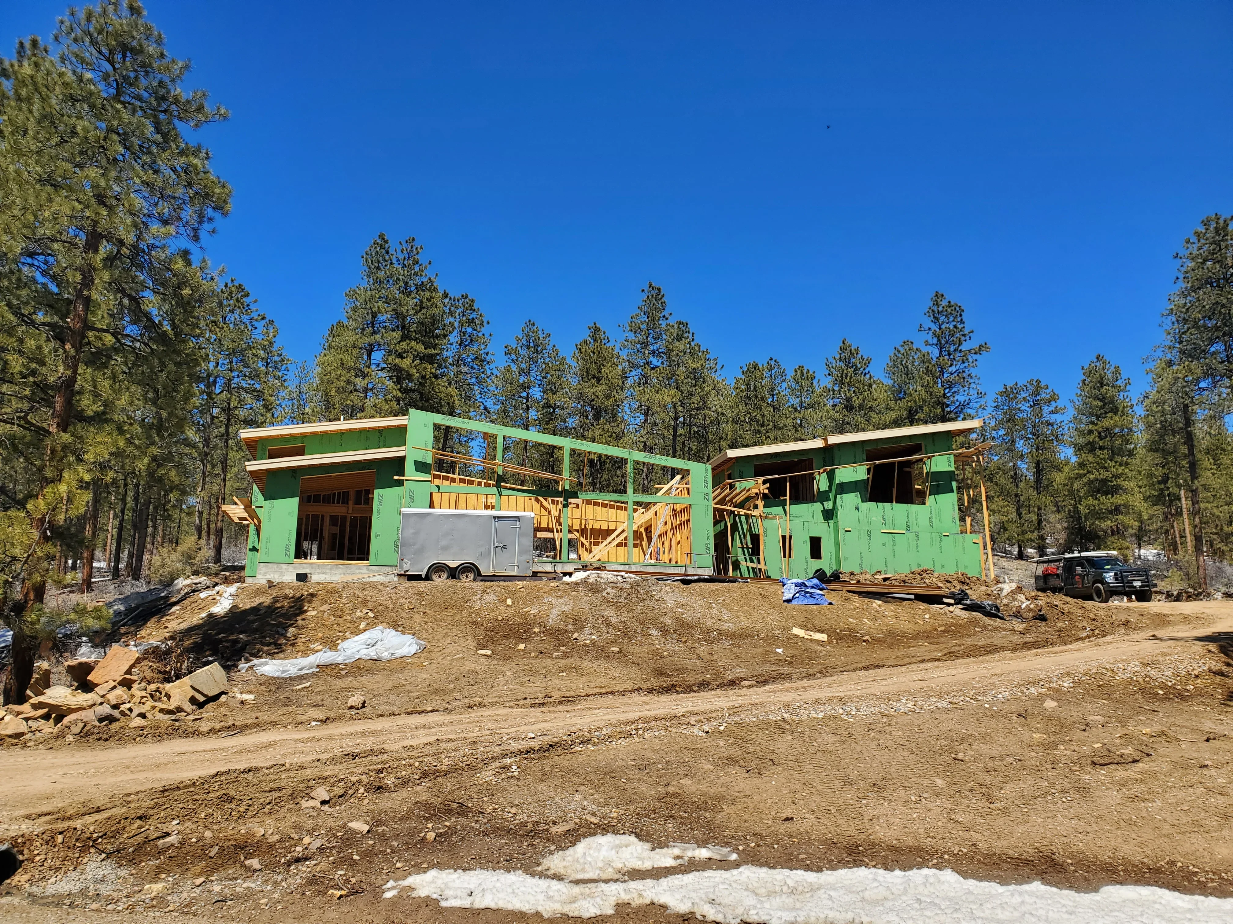 Green steel frame residential structure with yellow lumber framing and metal decking under construction