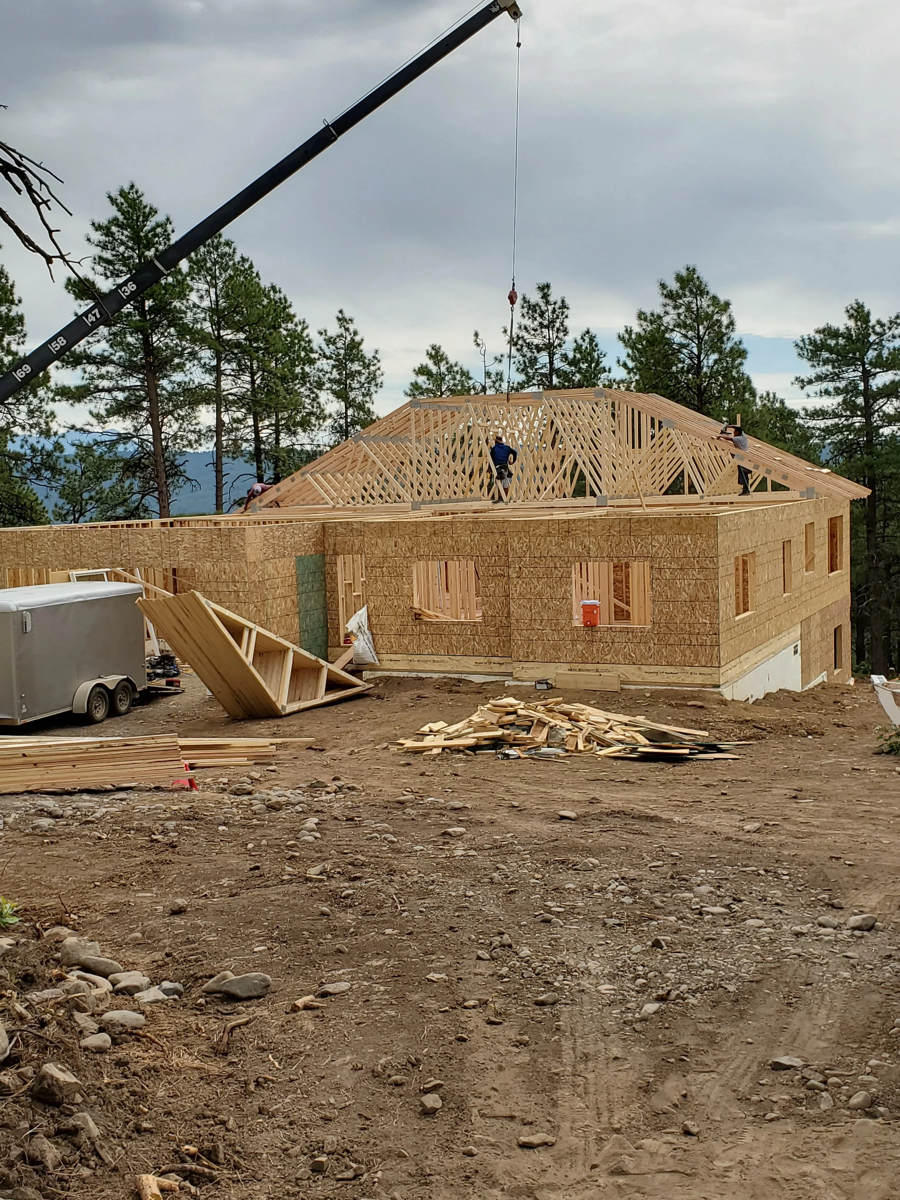 Wood-framed residential home under construction with OSB sheathing, roof trusses, and crane placement